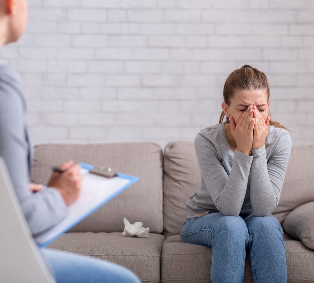 Mental health and psychological help concept. Young woman with depression on counseling session with therapist at clinic. PTSD disorder, anxiety, emotional problems treatment